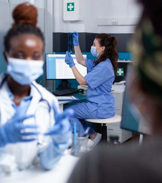 Nurse with ct scan during doctor visit Background focus on nurse wearing protective mask and gloves checking clinical x-ray ct scan results during doctor - patient social distancing medical check-up in sanitary sterile clinic
